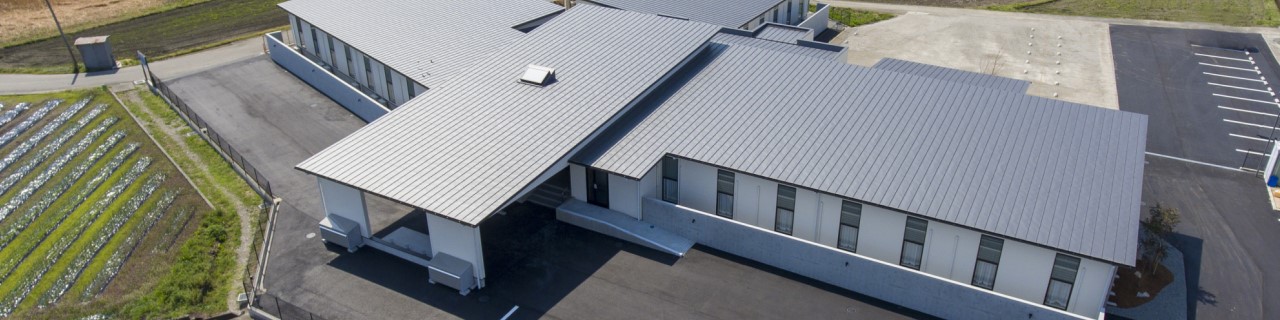 白い屋根の平屋建て介護施設の外観。駐車場と周辺環境が見える